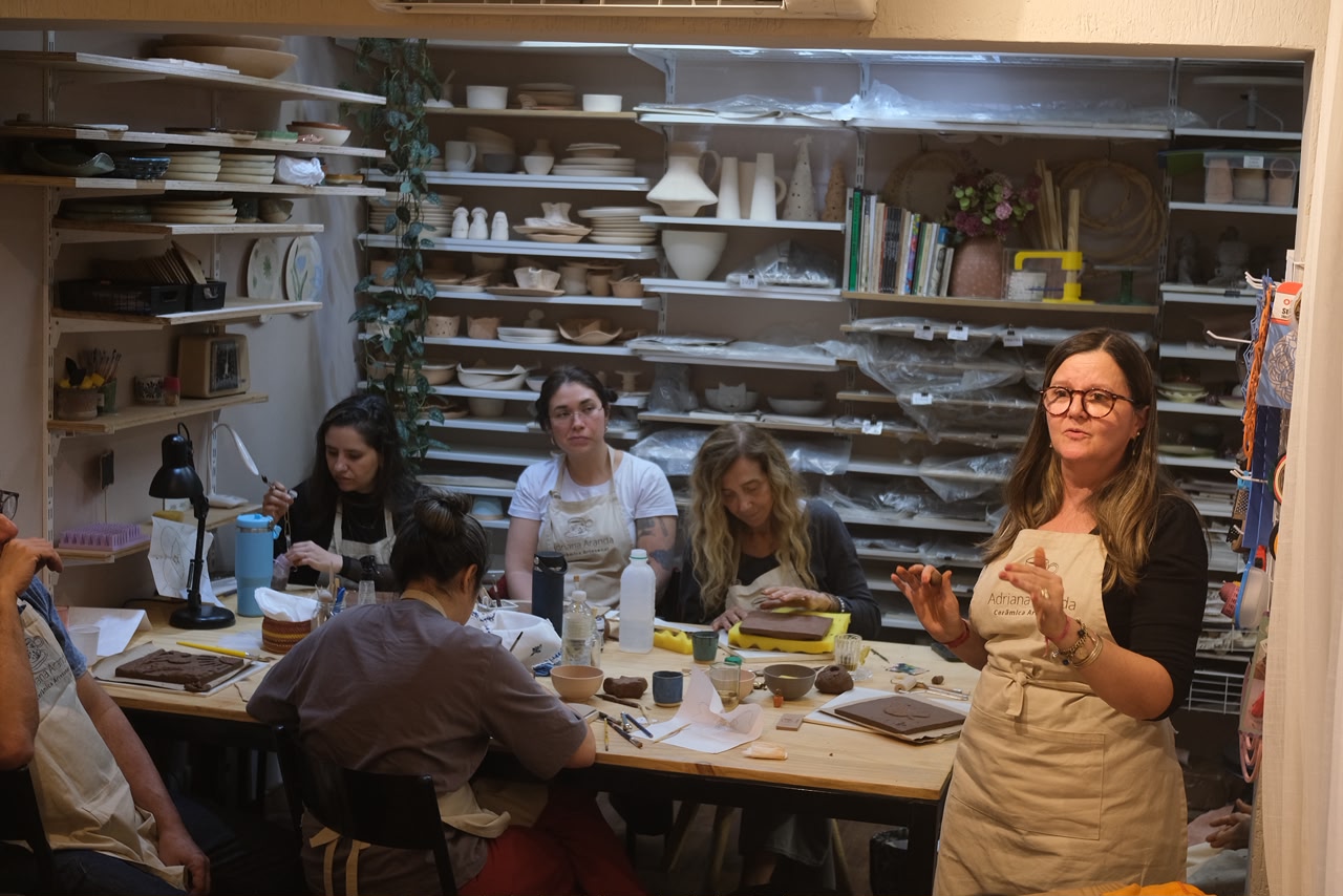 Turma de alunas em aula no ateliê, com a Adriana explicando ao lado da mesa